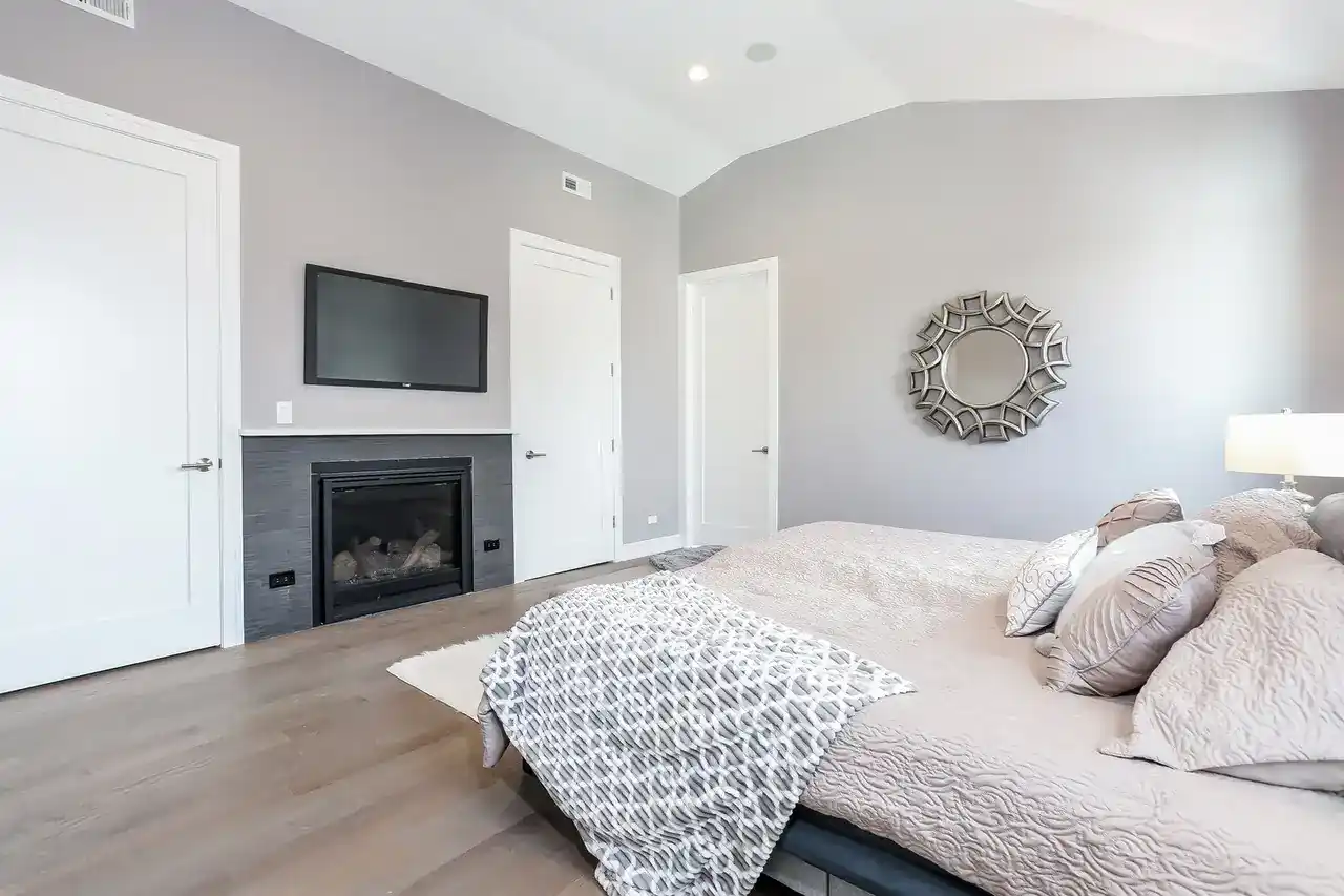 Primary bedroom with vaulted ceiling, gas fireplace with mounted TV, and round decorative mirror