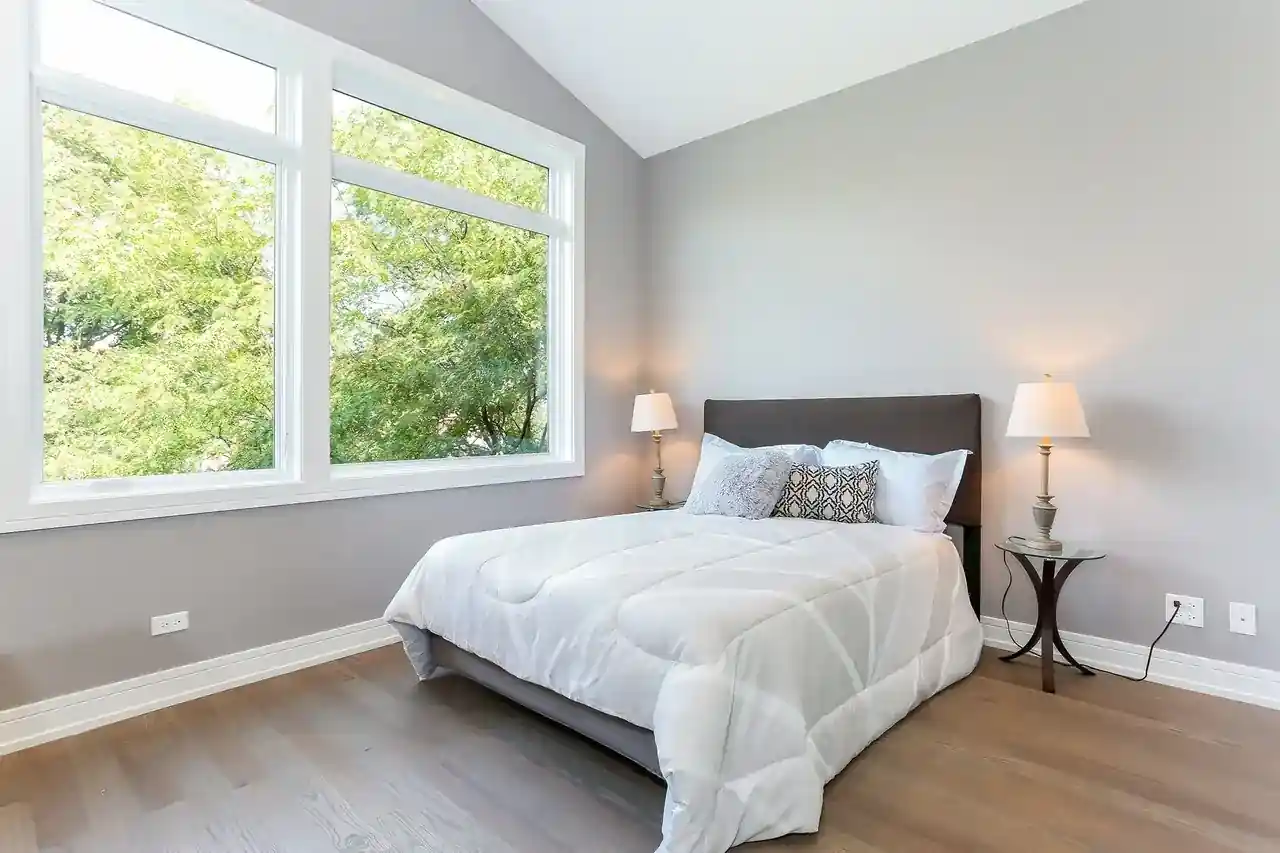 Bedroom with dark upholstered headboard, large window overlooking trees, and wood flooring