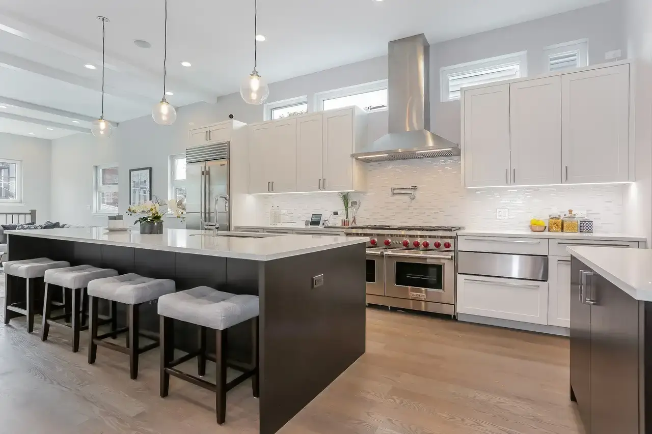Kitchen with white shaker cabinets, dark waterfall island, stainless range hood, and pendant lighting