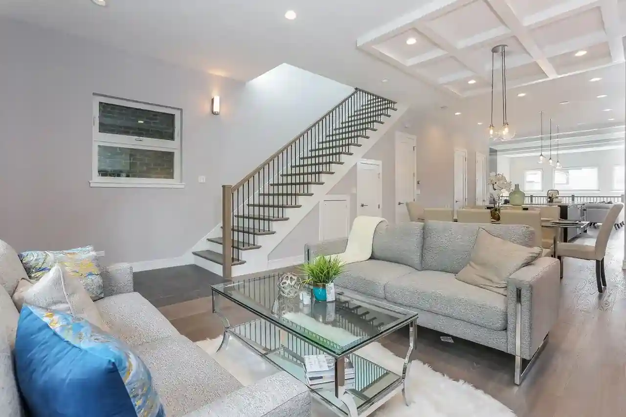 Living room with floating staircase, coffered ceiling, glass coffee table, and open dining area beyond