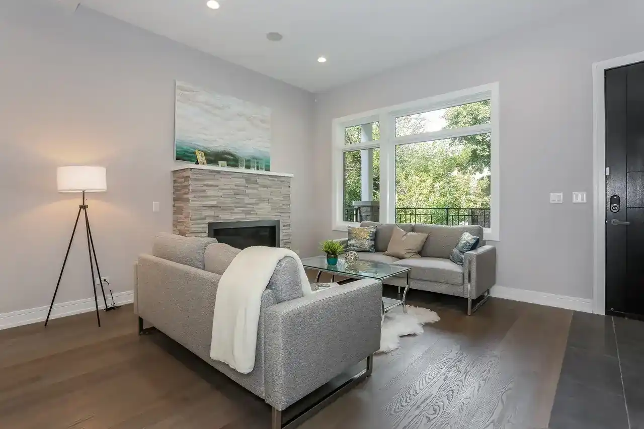 Living room with stone fireplace, gray sectional sofa, floor lamp, and large windows to balcony