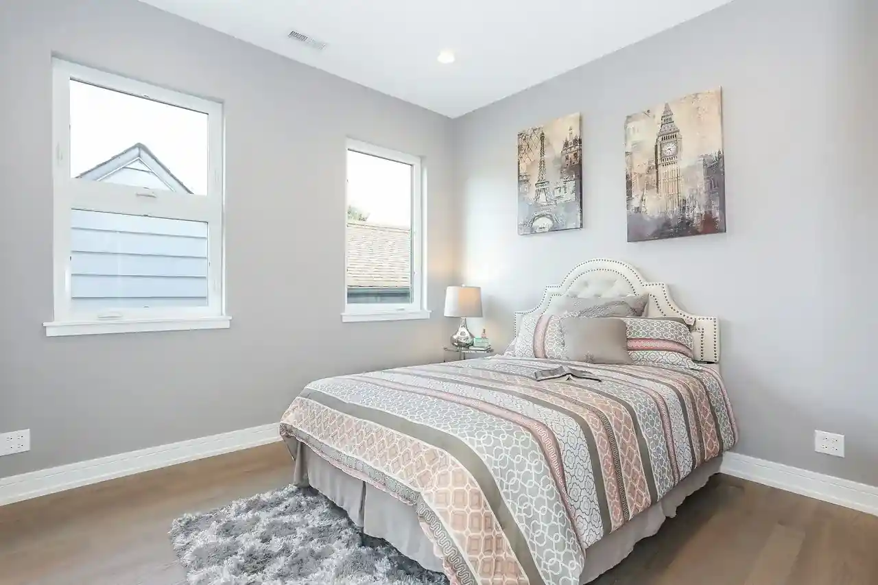 Bedroom with striped upholstered bed, framed travel art above headboard, and dual windows