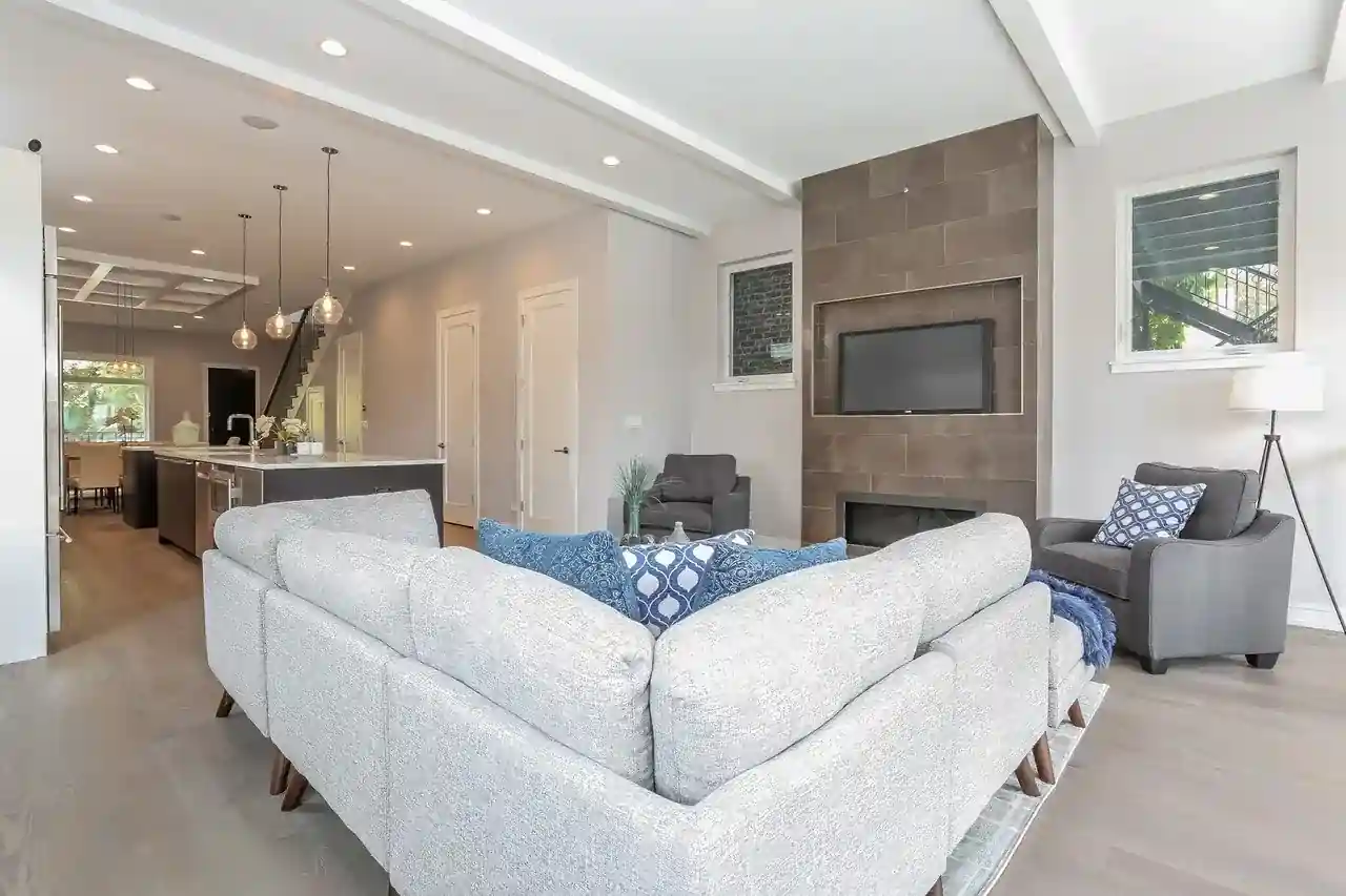 Upper-level family room with tiled fireplace wall, mounted TV, and sectional sofa overlooking kitchen