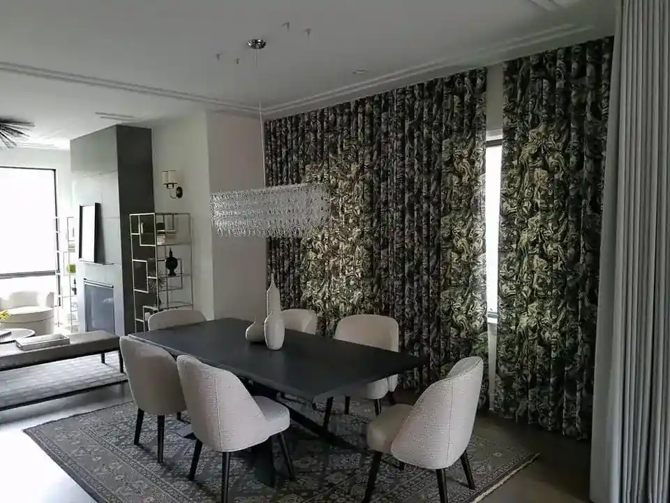 Dining area with a statement crystal chandelier, patterned drapery, and upholstered chairs around a dark wood table