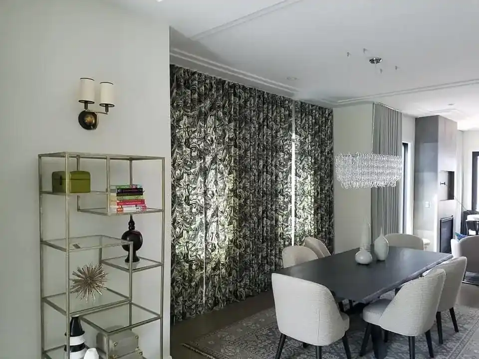 Living and dining area with floor-to-ceiling patterned drapery, crystal chandelier, and glass display shelving