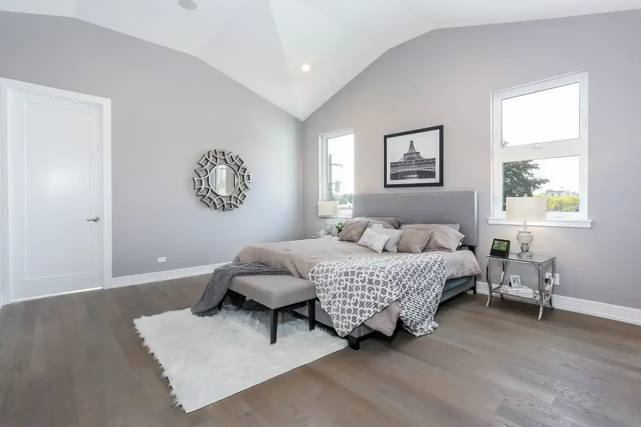 Primary bedroom with upholstered gray headboard, round mirror, and framed Eiffel Tower print