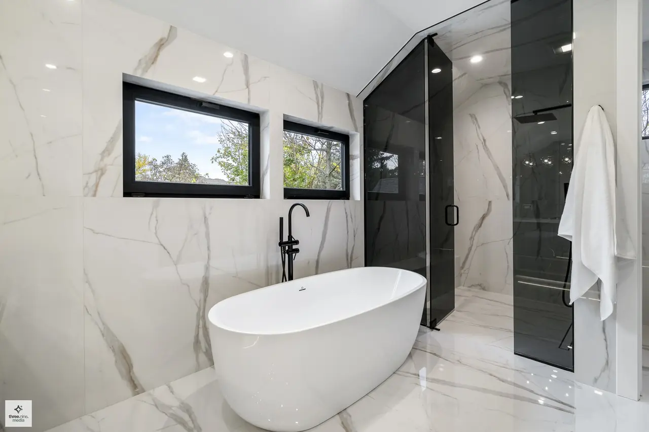 Primary bathroom tub nook framed by dual windows and a glass shower wall