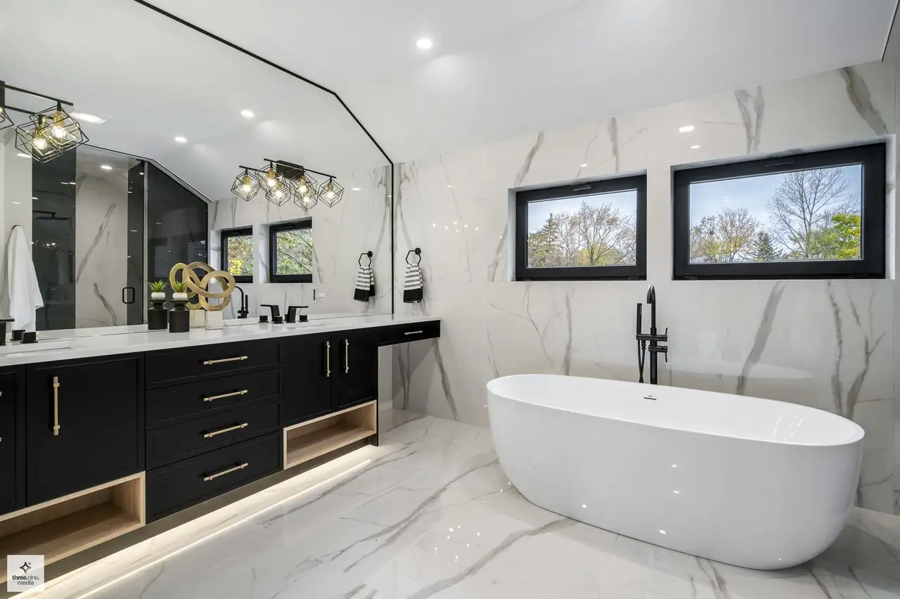 Primary bathroom with a black vanity, marble slab walls, and freestanding tub