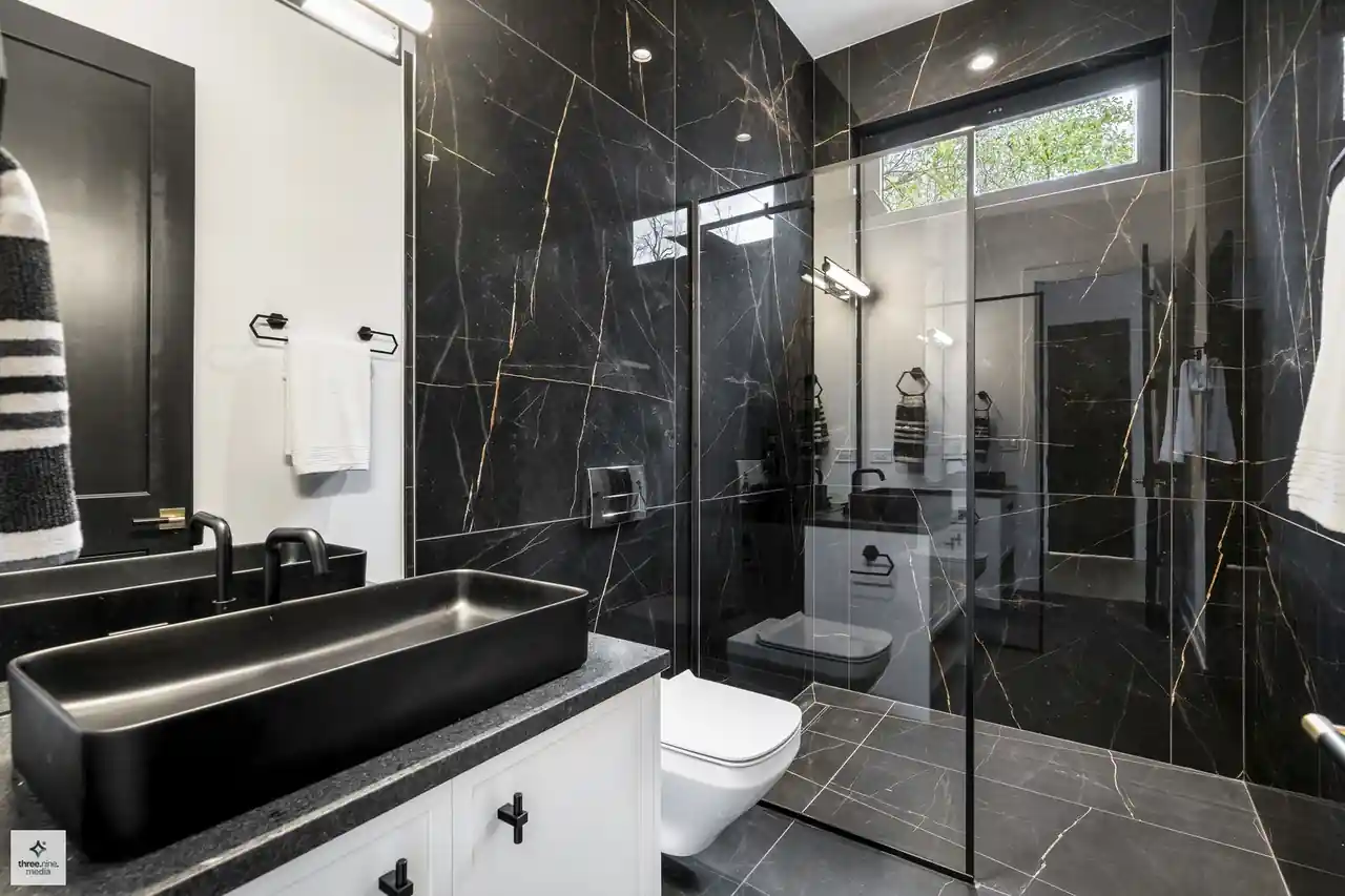 Bathroom with a black marble slab shower, floating toilet, and vessel sink