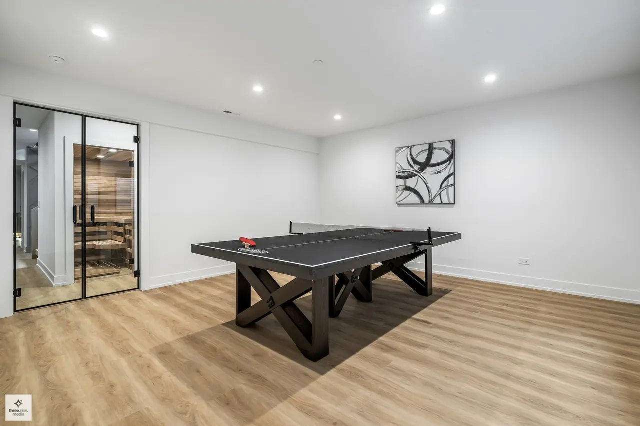 Recreation room with a ping pong table and glass-enclosed sauna beyond