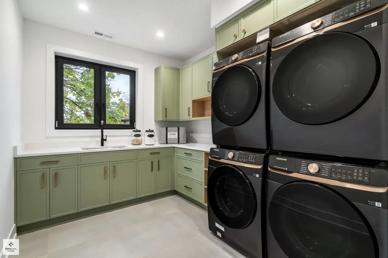 Laundry room with sage green cabinetry and a stacked front-load washer and dryer