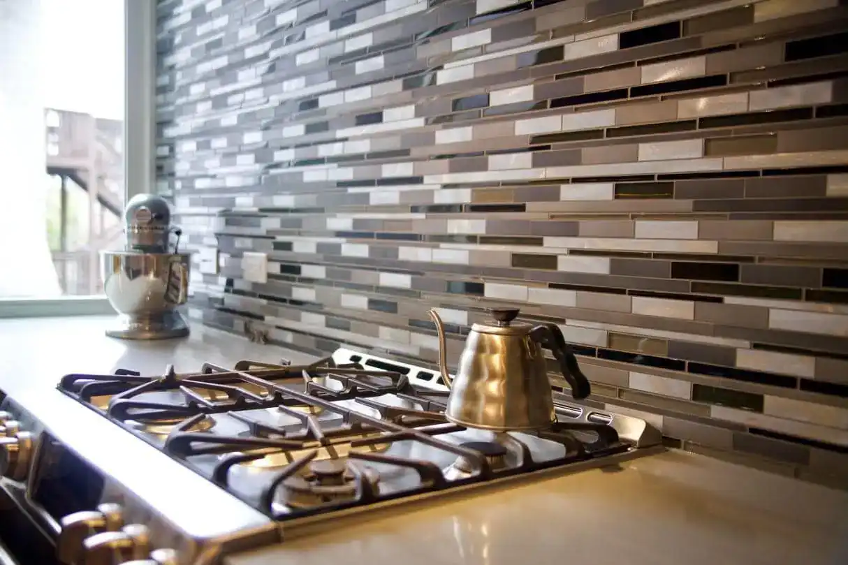 Close-up of mosaic glass tile backsplash with gas range and pour-over kettle in a Rice multifamily unit kitchen