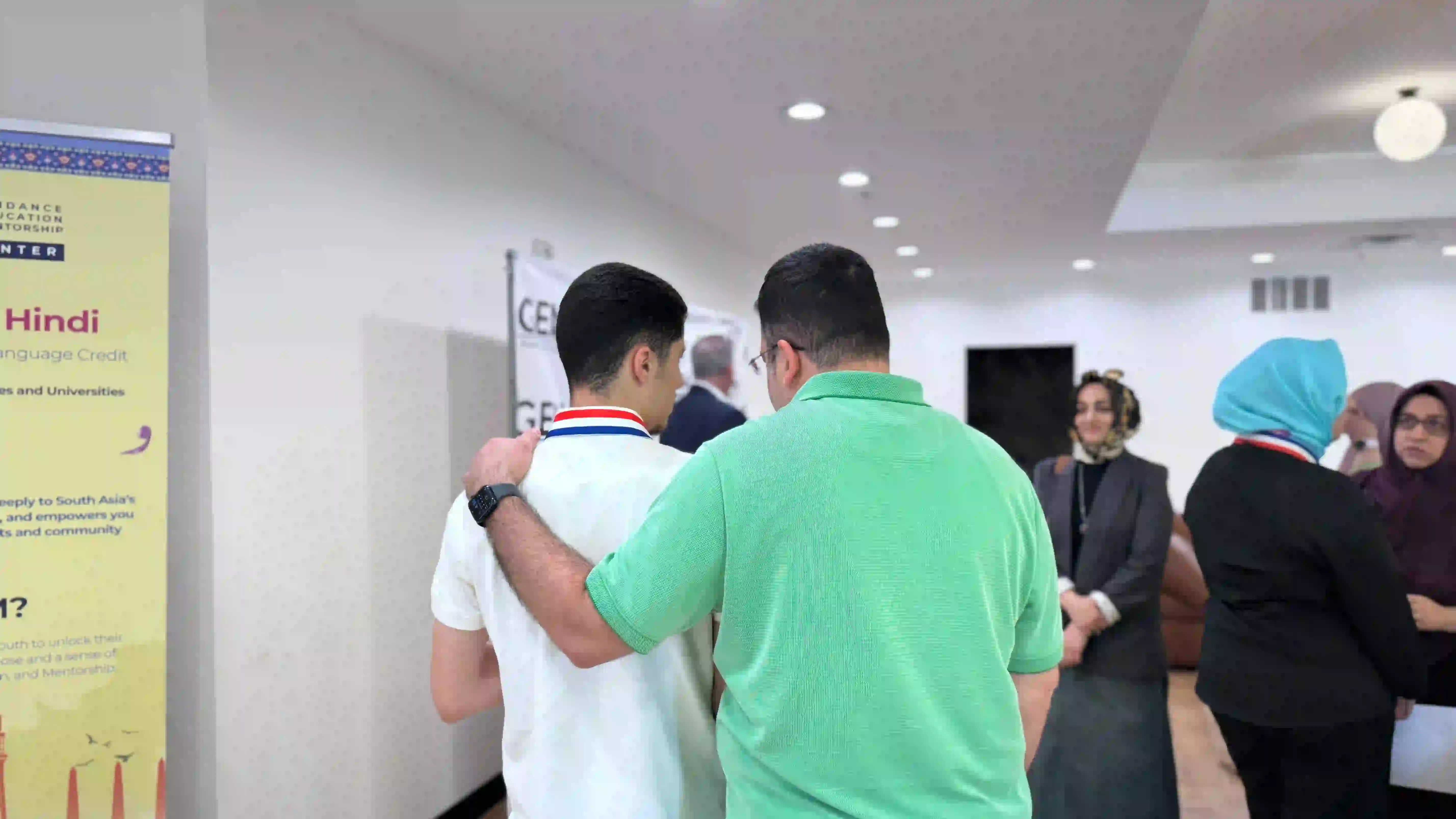 two young men hugging while two women stand nearby in indoor space