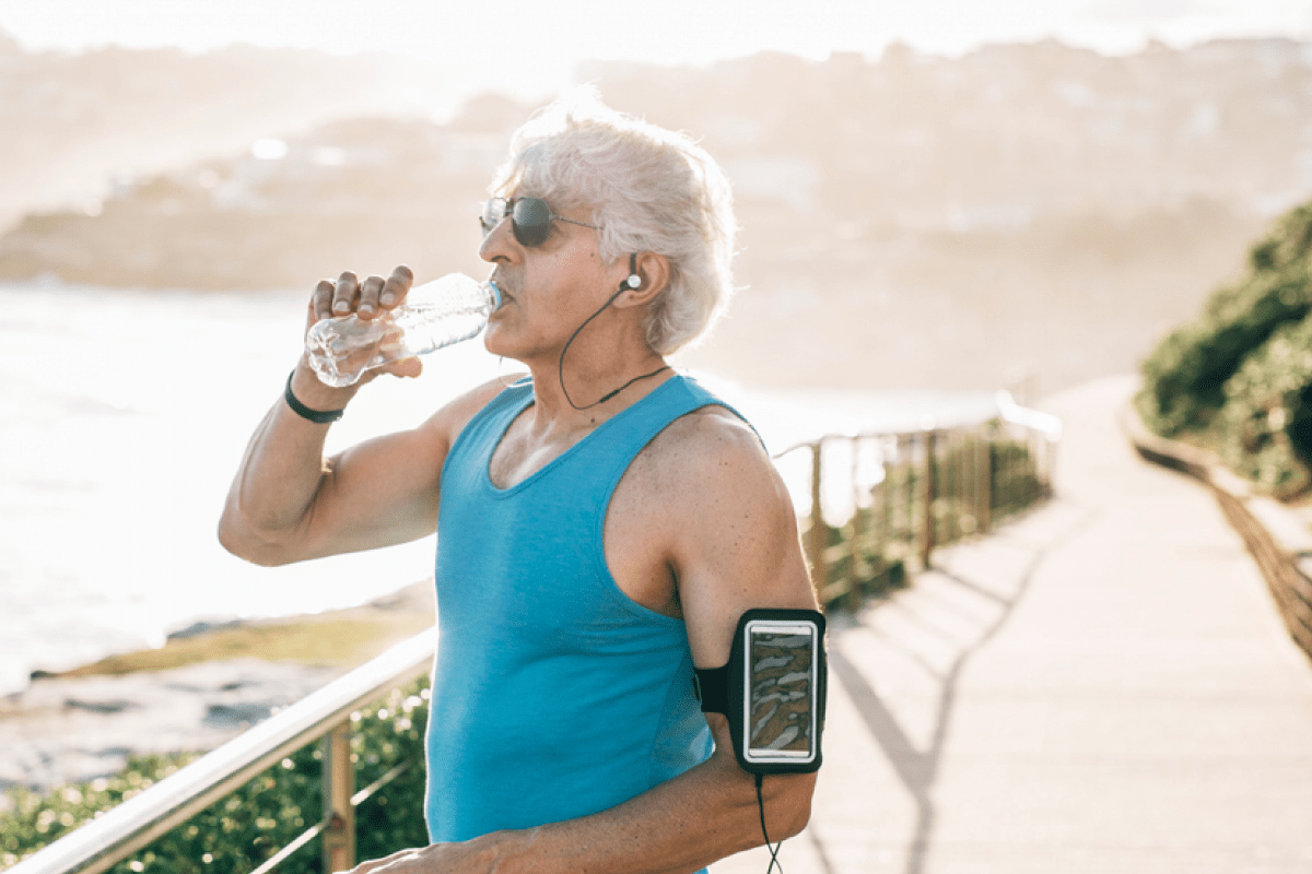 Fit elderly man taking a break from his run to drink water.