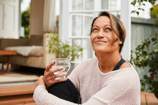 Smiling woman holding a glass of water, reflecting gut-brain connection wellness.