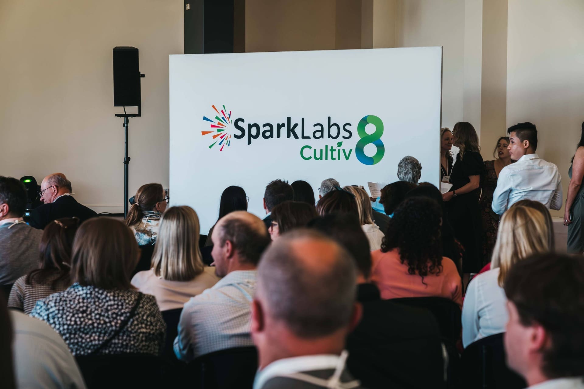 Audience facing a large board with the SparkLabs Cultiv8 logo in a conference room.