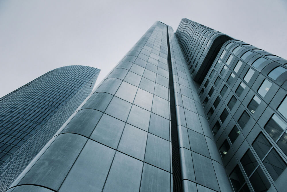 Low-angle view of three modern skyscrapers with glass and metal facades against a gray sky.