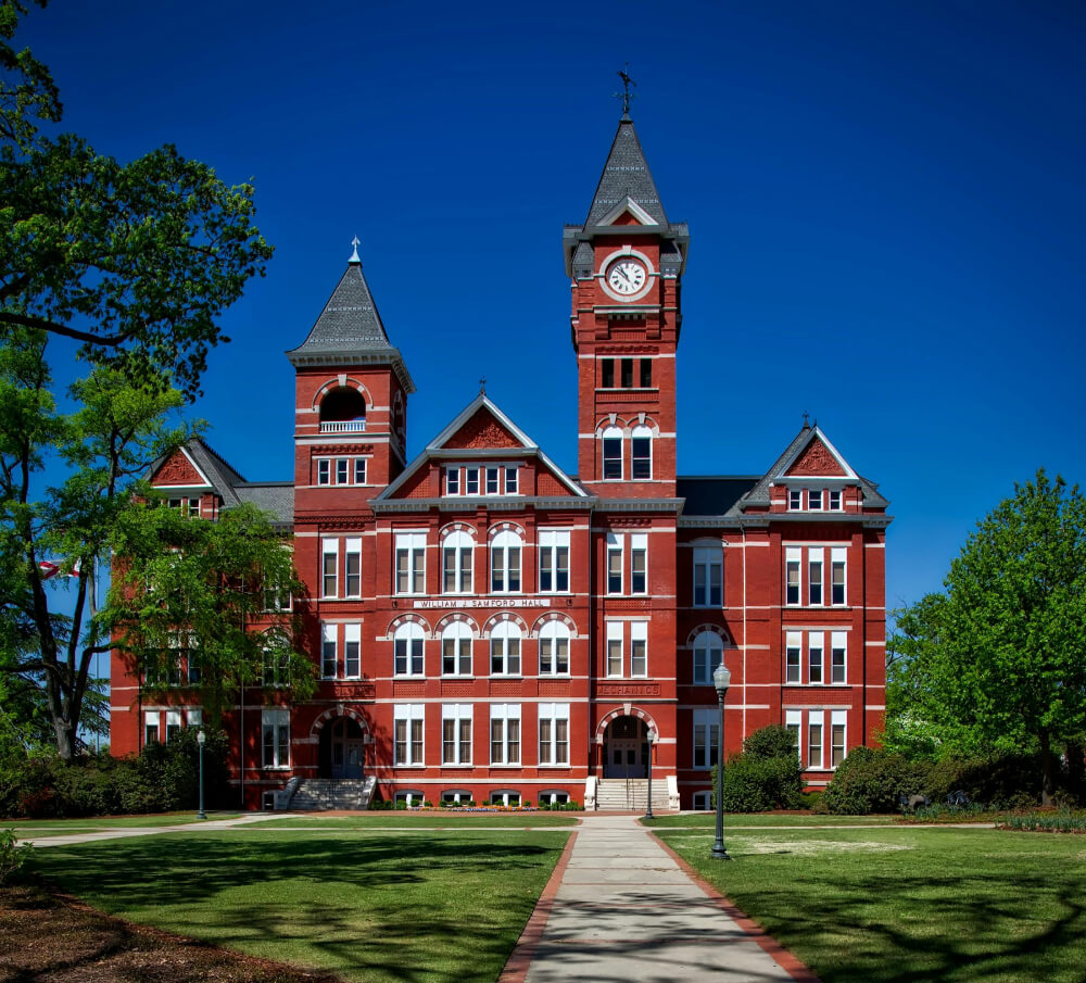 William R. Samford Hall, a historic red brick building with a clock tower, on Auburn University campus under clear blue sky.