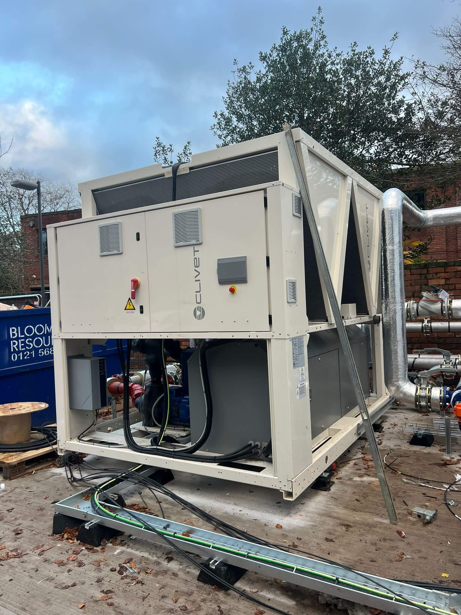 Large Clivet HVAC unit installed outdoors with visible pipes and electrical cables on a concrete platform.