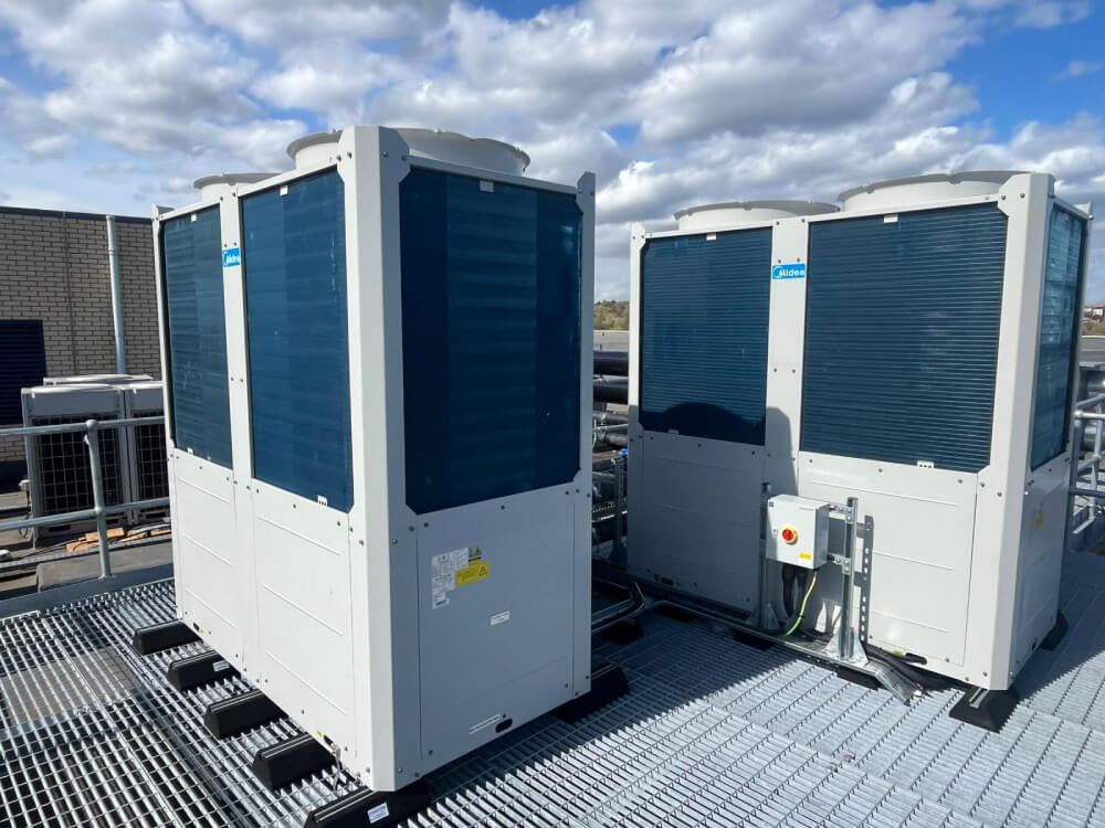 Two large industrial air conditioning units on a metal rooftop platform under a partly cloudy sky.