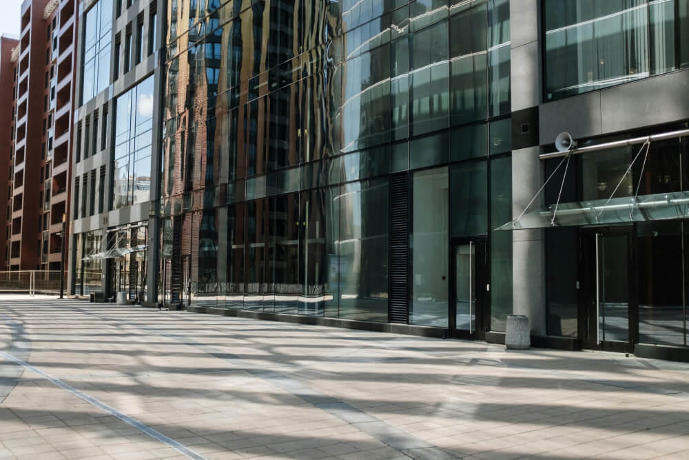 Empty urban plaza with modern glass office buildings reflecting surrounding structures on a sunny day.