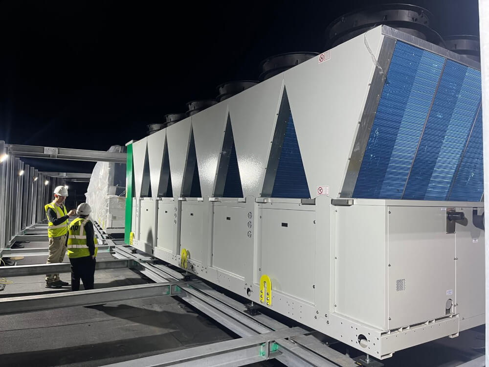 Two ICG engineers wearing helmets and reflective vests inspecting large industrial HVAC units at night.