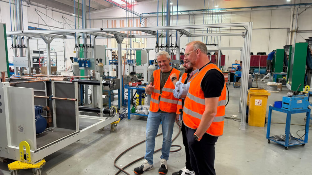 Three ICG engineers standing and discussing inside a large industrial workshop with machinery and equipment.
