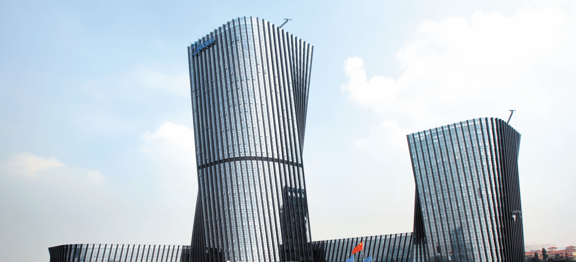 Two modern, twisting skyscrapers with glass facades under a clear sky and flags at the base.