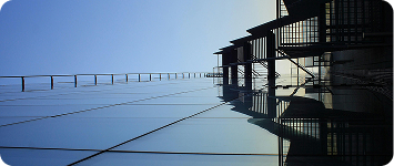 Modern glass building facade reflecting blue sky with metal structural elements.