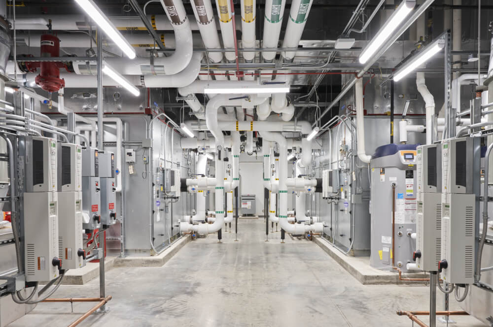 Symmetrical industrial room with numerous white pipes and machinery for heating and cooling systems.