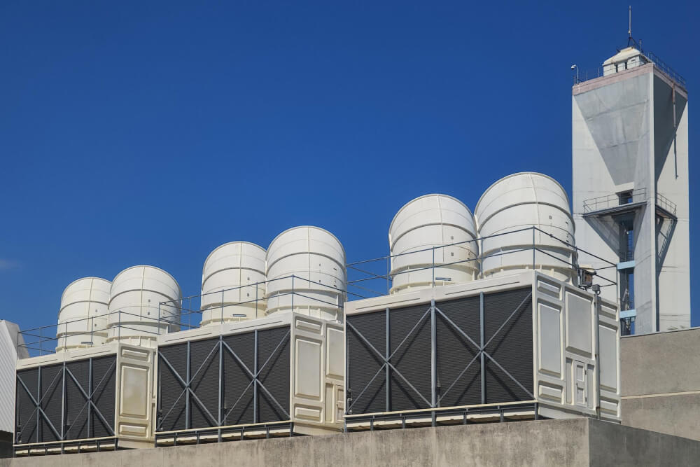 Large industrial cooling units with cylindrical tops on a rooftop under a clear blue sky.