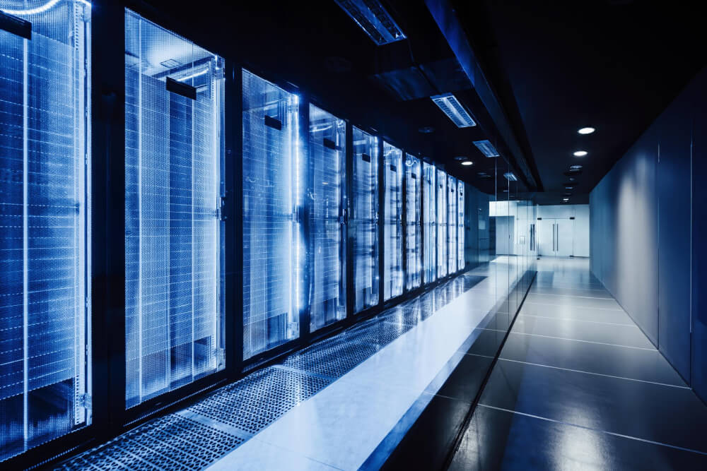 Row of illuminated server racks in a modern data center corridor with reflective floors and glass walls.