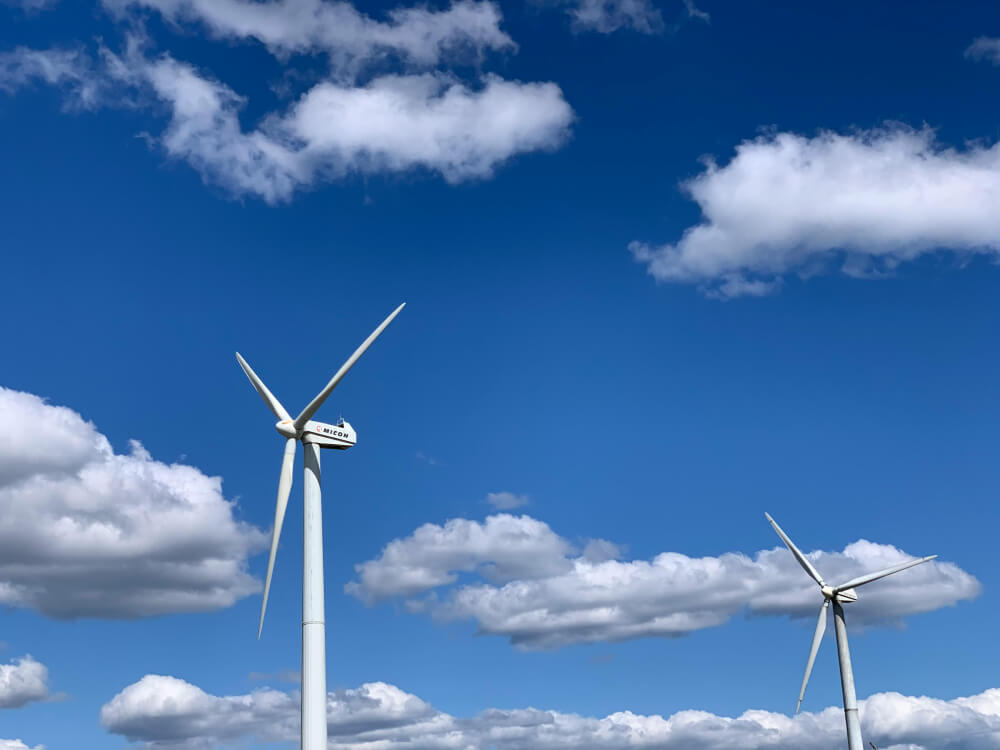 Two tall white wind turbines against a blue sky with scattered white clouds.