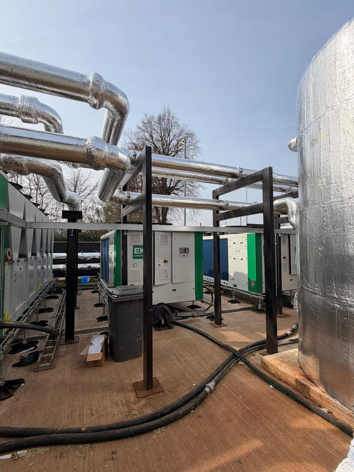 Outdoor industrial HVAC units with interconnected insulated pipes and metal framework under a clear sky.