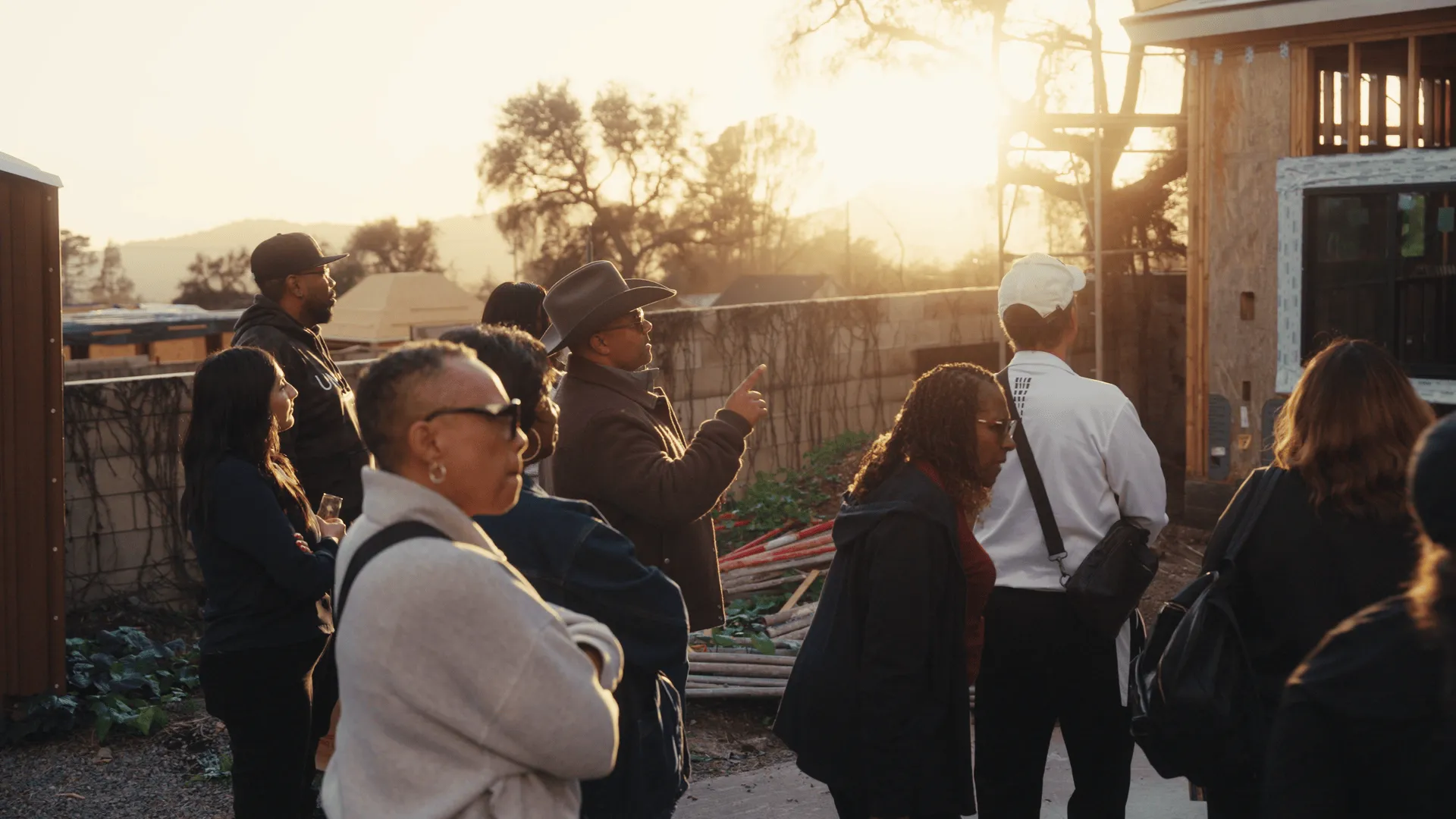 Group of people observing a construction site outdoors at sunset.