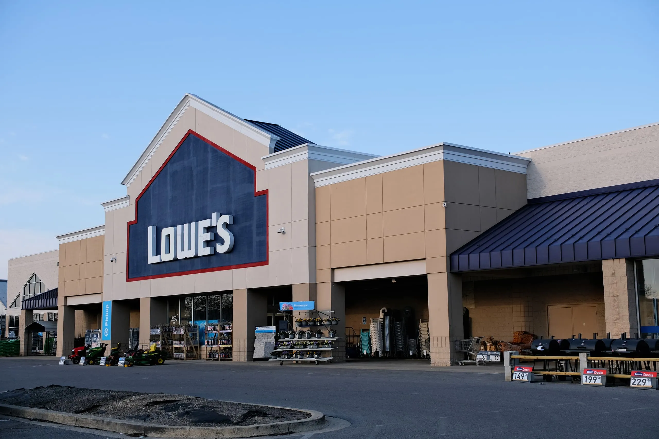 Exterior view of a Lowe's home improvement store with displayed lawn mowers, plants, and grills outside.