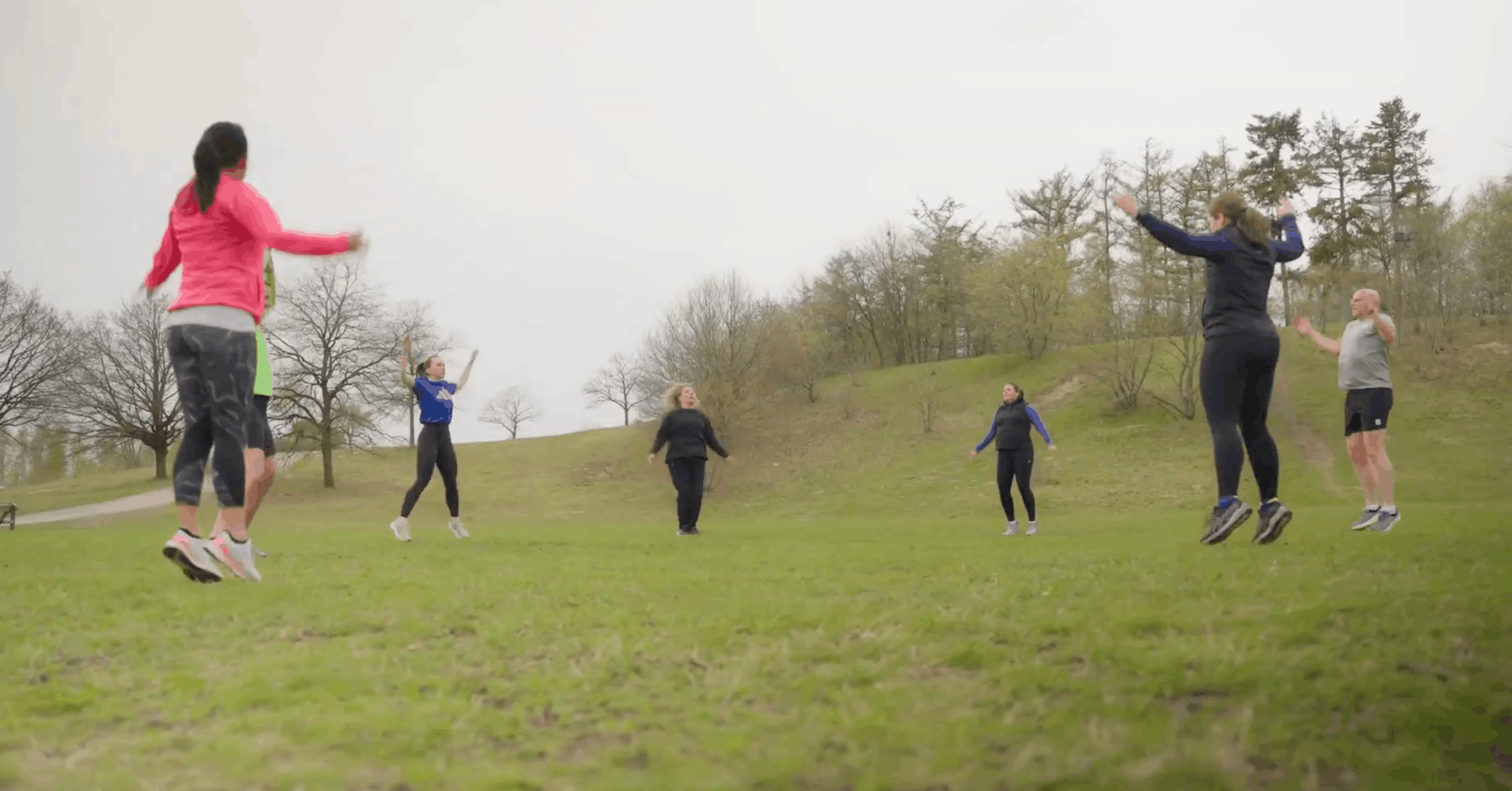 Gruppe von Menschen macht Sprungübungen auf einer grünen Wiese im Freien.