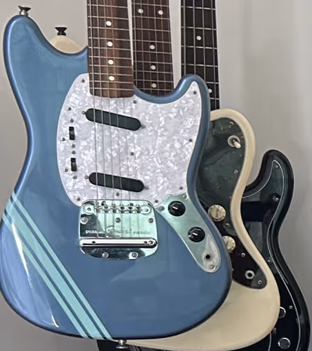 Trois guitares électriques accrochées, avec une guitare bleue à l'avant, une guitare blanche au milieu et une guitare noire à l'arrière.