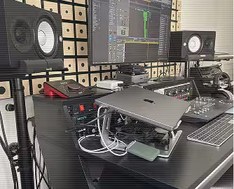 Bureau de studio de musique "la crème anglaise" avec haut-parleurs, écran d'ordinateur affichant un logiciel audio, ordinateur portable ouvert et clavier.