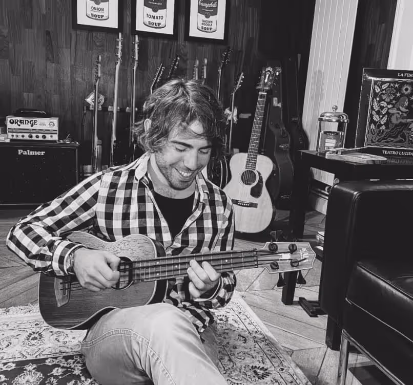 Geoffrey Guennec fondateur du studio de musique "La Crème Anglaise" qui joue de la guitare assis par terre dans une pièce avec plusieurs guitares et amplificateurs en arrière-plan.