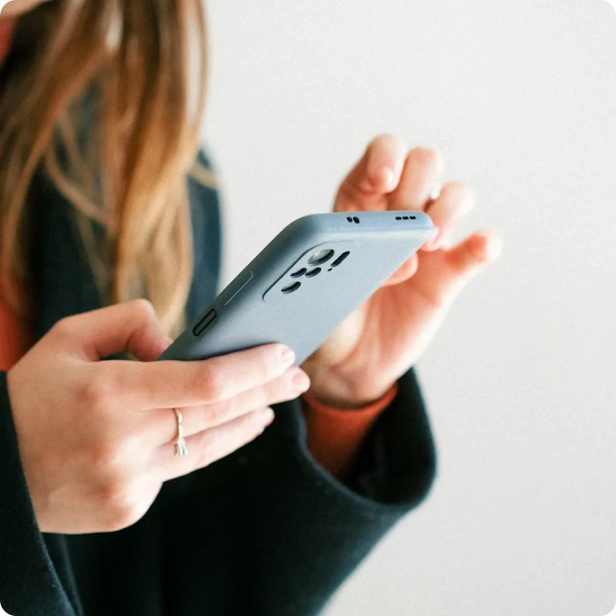 Person mit langem Haar benutzt ein Smartphone mit grauer Hülle vor hellem Hintergrund.