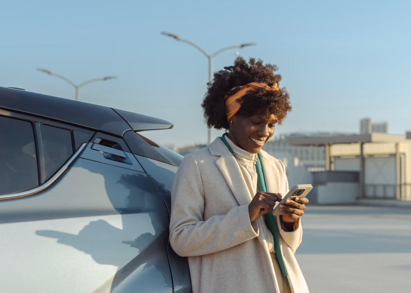 Woman standing beside a car and smiling while using the Self Inspection app on her smartphone.
