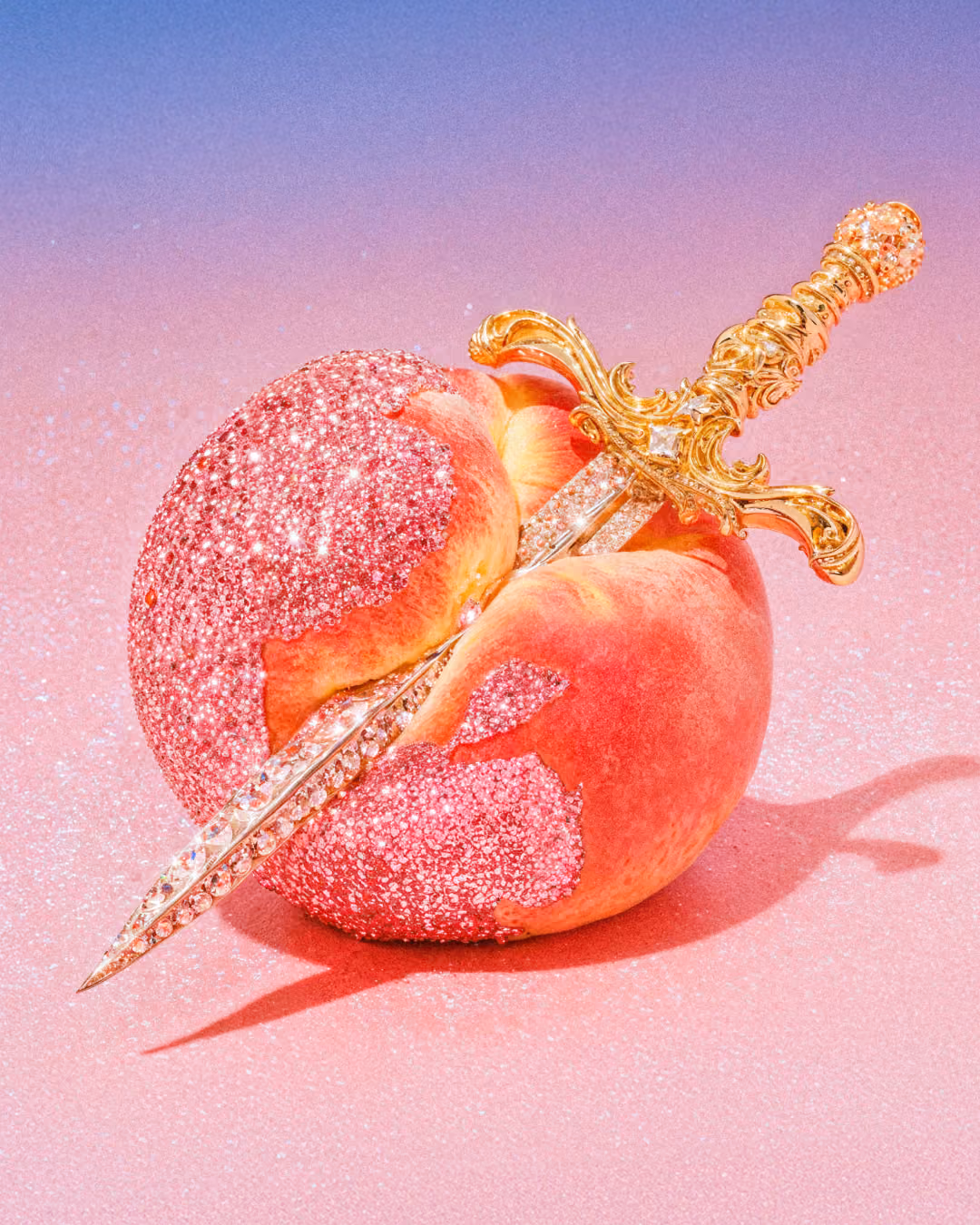 A ripe peach covered in pink glitter, pierced diagonally through the center by an ornate gold and crystal dagger against a soft pink background.