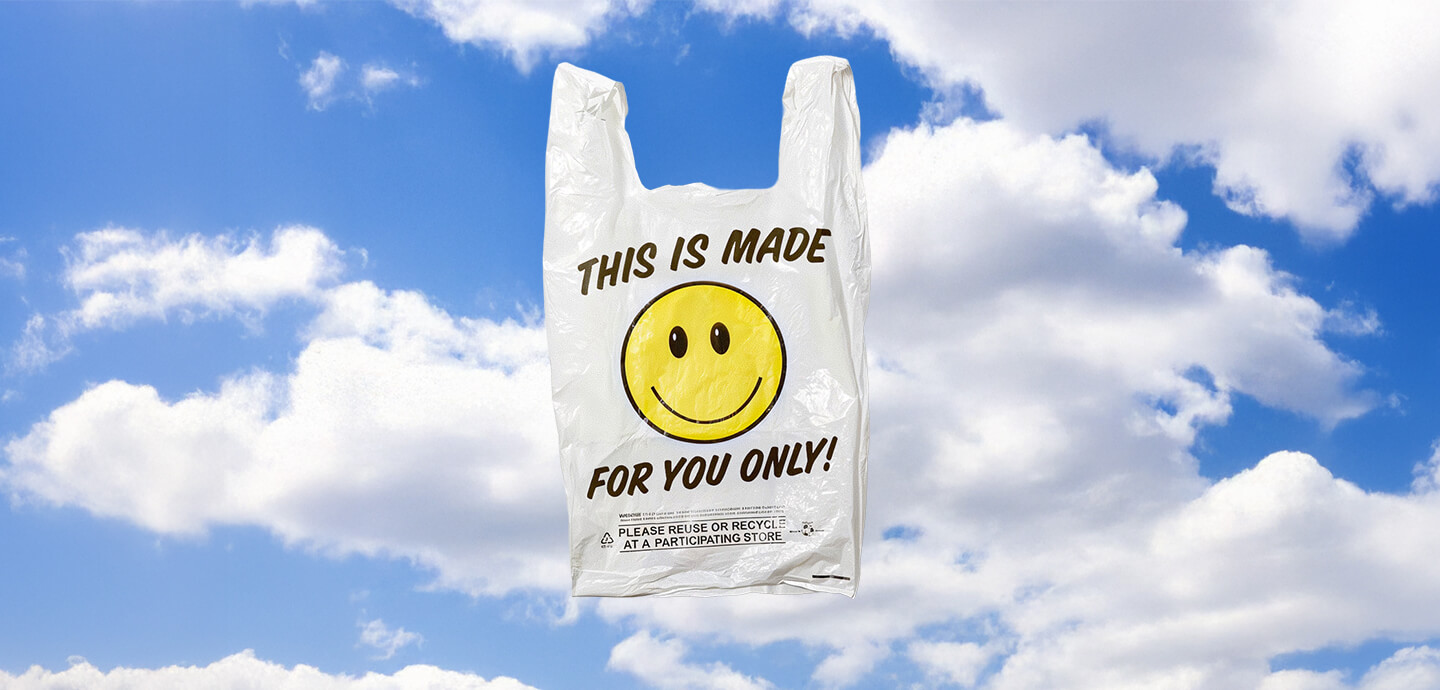 A white plastic grocery bag floating against a blue sky with fluffy clouds, printed with a yellow smiley face and the text "THIS IS MADE FOR YOU ONLY!".