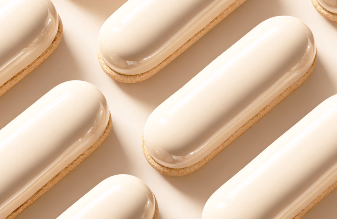 A repeating diagonal pattern of glossy cream-colored, capsule-shaped pastries sitting on light biscuit bases over a beige background.