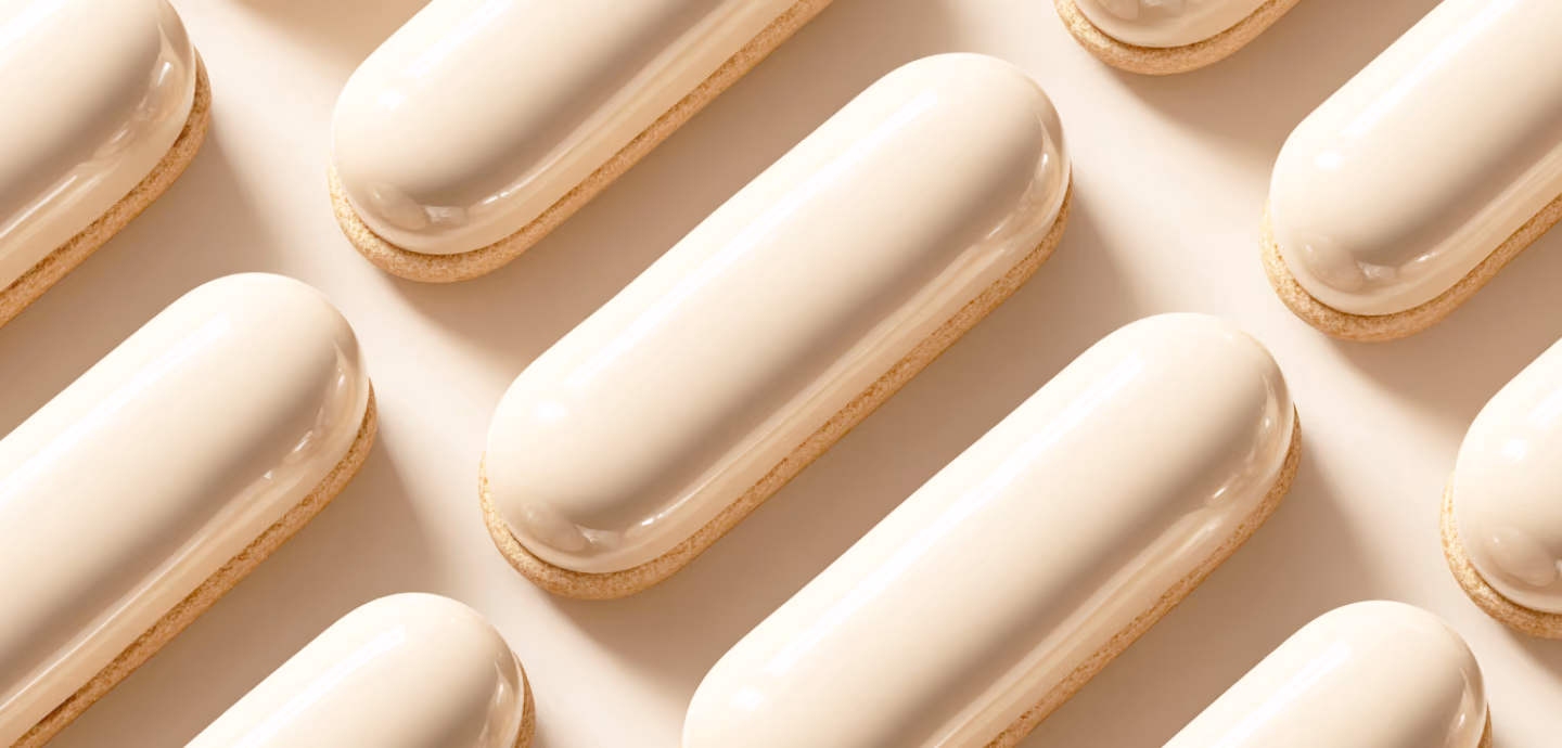 A repeating diagonal pattern of glossy cream-colored, capsule-shaped pastries sitting on light biscuit bases over a beige background.