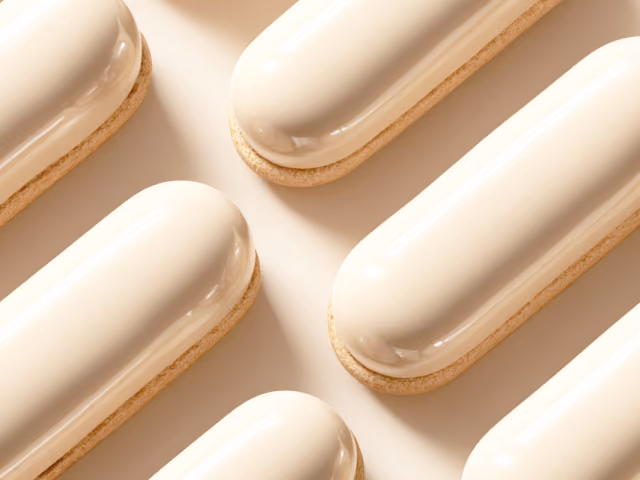 A repeating diagonal pattern of glossy cream-colored, capsule-shaped pastries sitting on light biscuit bases over a beige background.