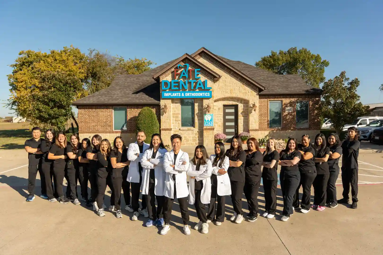 Group of dental staff and doctors standing confidently in front of Fate Dental Implants & Orthodontics building.