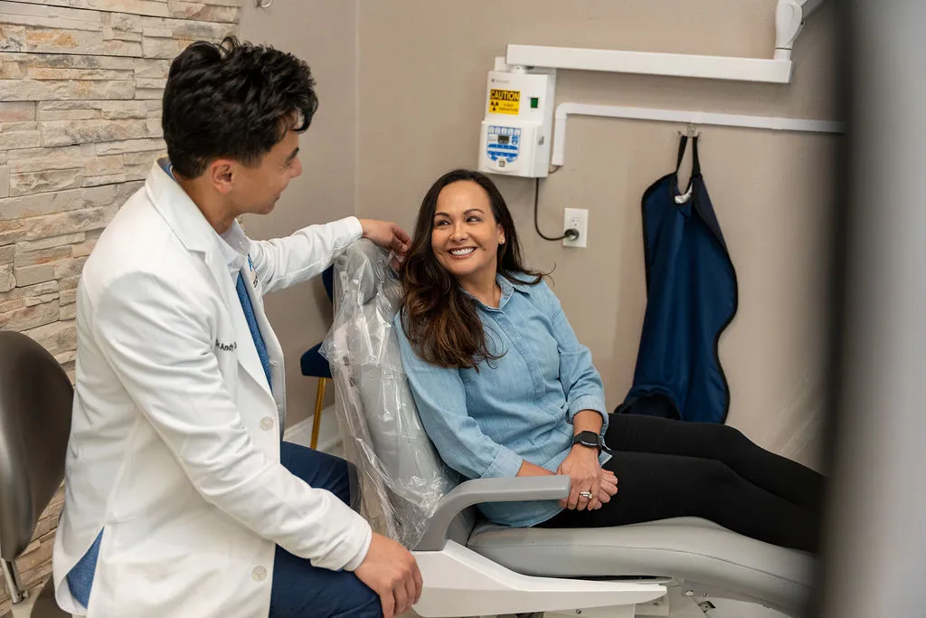 Smiling female patient sitting in dental chair talking with male dentist in white coat.