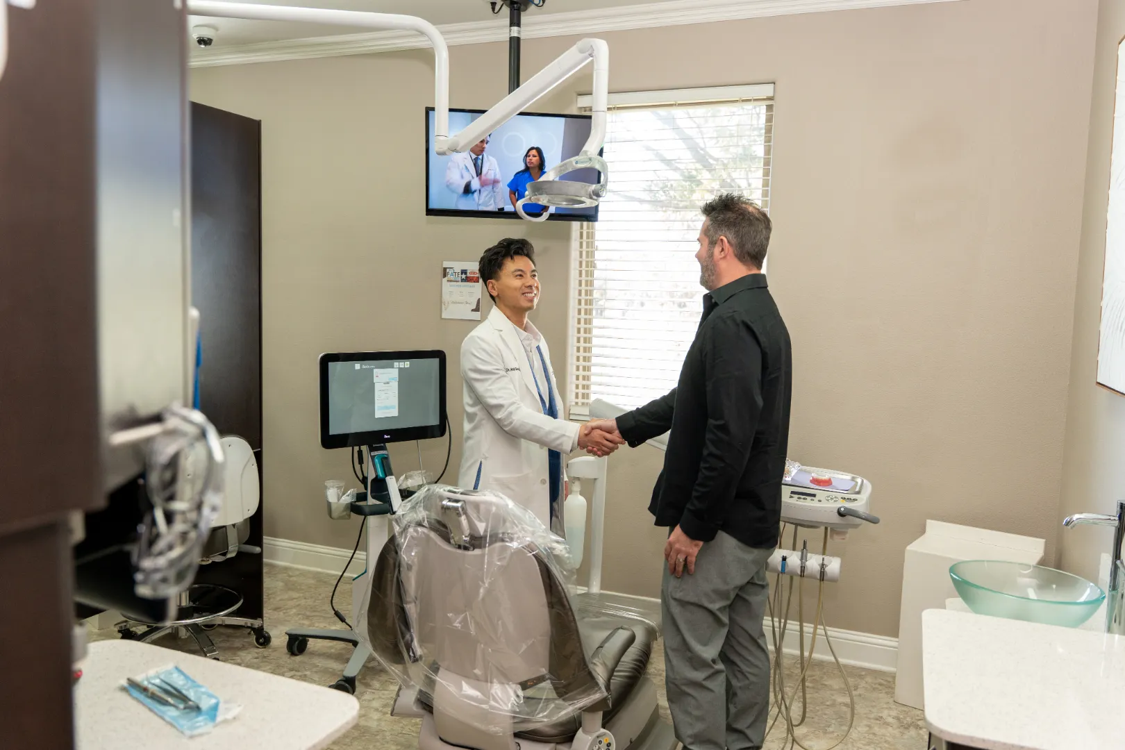 Dentist in a white coat shaking hands with a patient in a dental office.